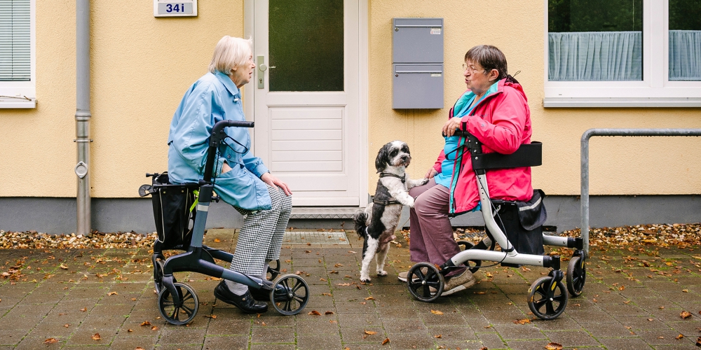 Zwei alte Damen unterhalten sich sitzend auf ihrem Rollator