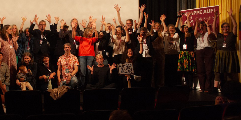 Gruppenfoto bei dem inklusiven Filmfestival Klappe auf!. Die Menschen strecken ihre Arme nach oben.