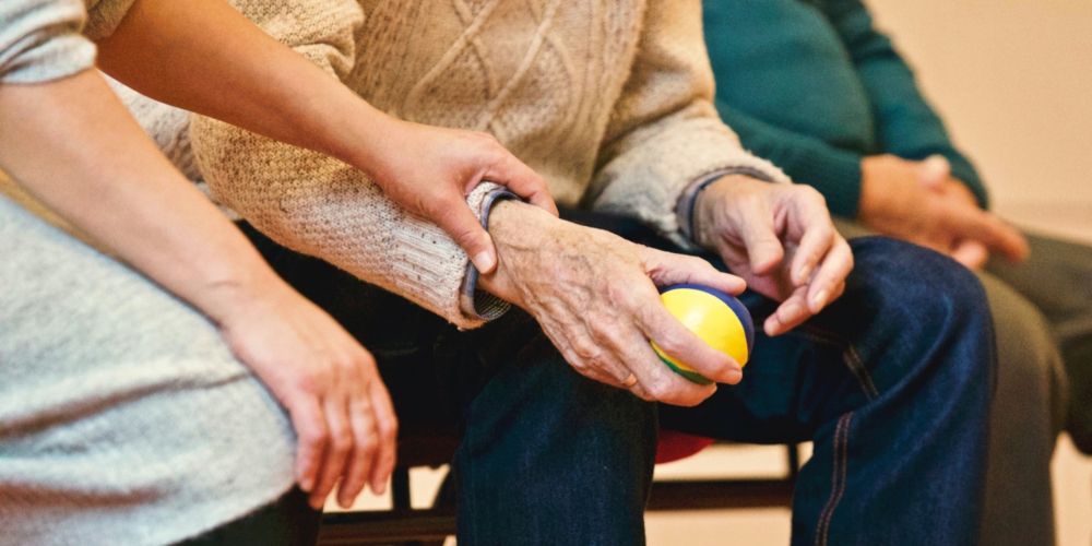Hände einer älteren Person. In der Hand hält die Person einen kleinen Ball.