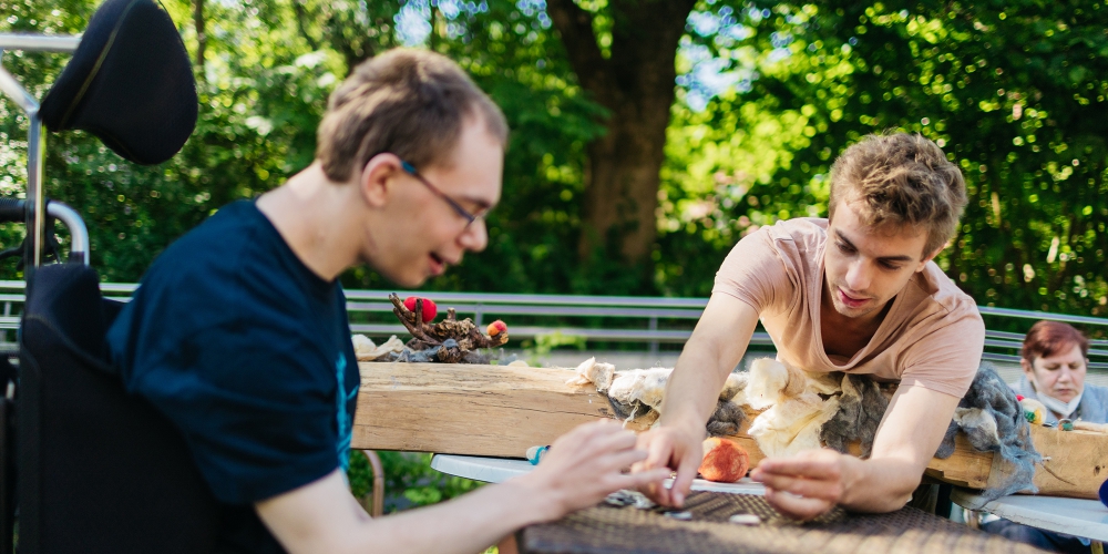 Zwei junge Männer basteln draußen mit Naturmaterialien.