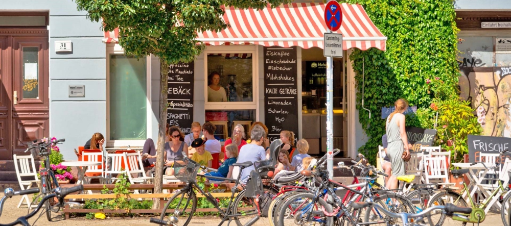 Mehrere Personen sitzen in der Sonne vor einem Café.