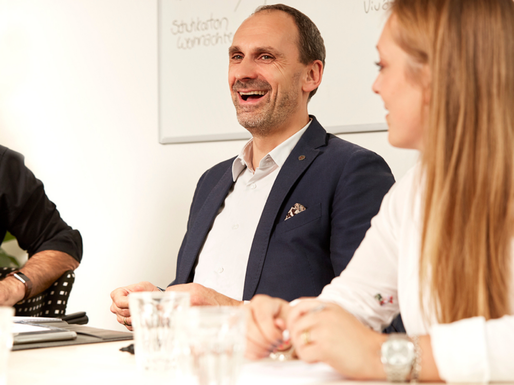 Geschäftsführer von careflex sitzt lachend an Konferenztisch.