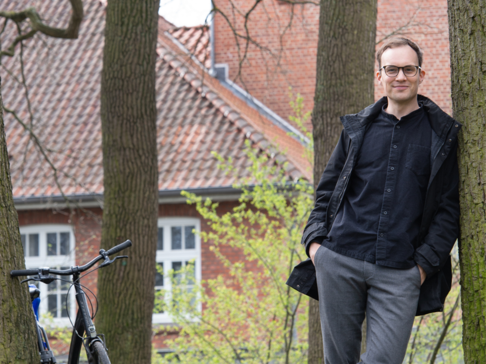 Nachhaltigkeitsreferent Alexander Rüther lehnt nehmen einem Baum, links sieht man sein Fahrrad.