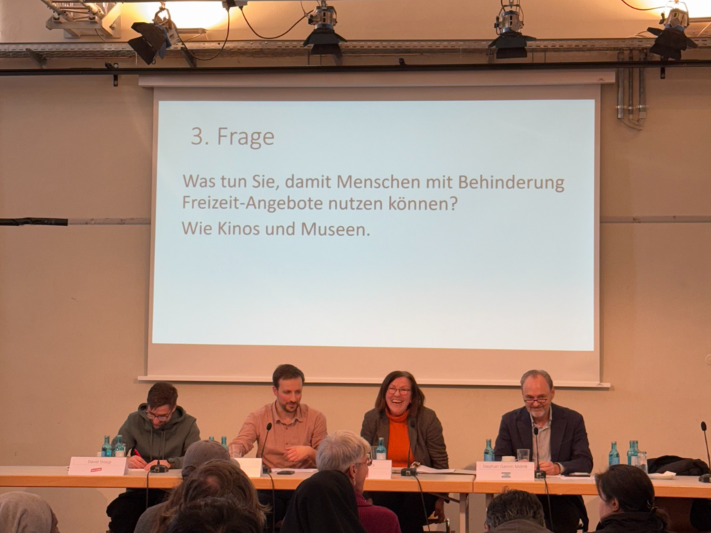 Vertreter*innen der Parteien sitzen auf dem Podium. Hinter Ihnen wir die Präsentation und aktuelle Diskussionsfrage projiziert.