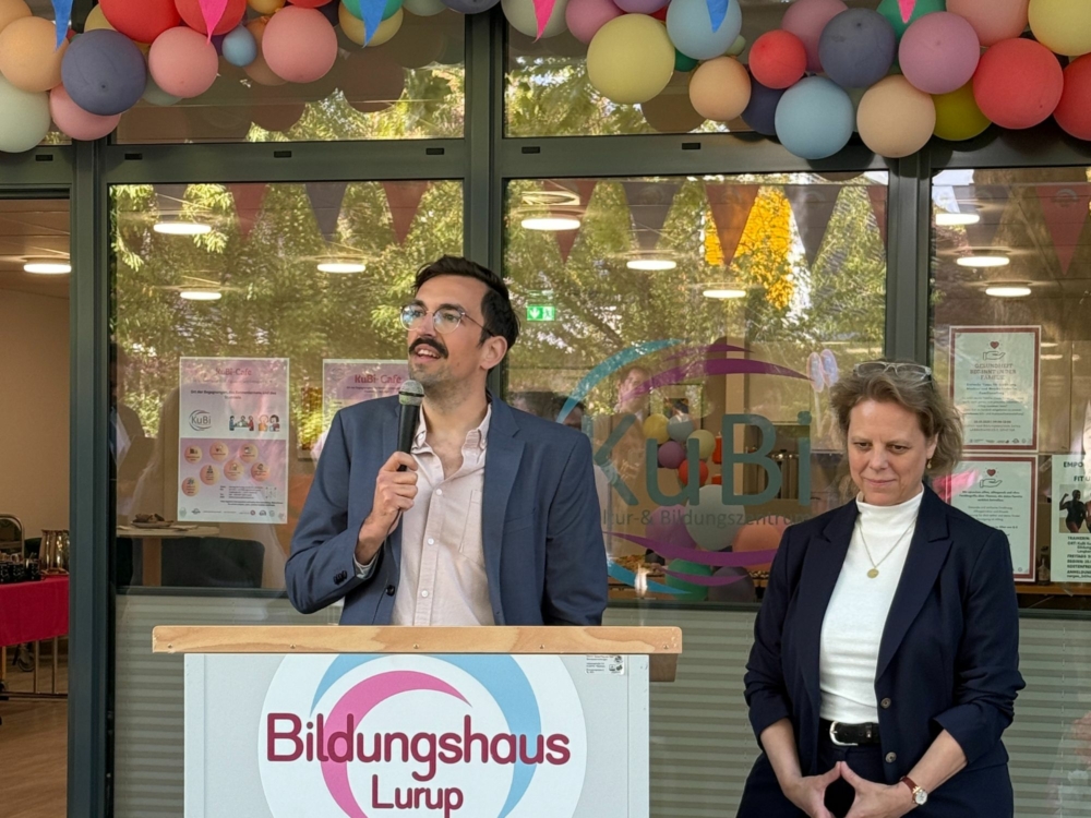 Ein Mann hält eine Rede hinter einem Podium. Neben ihm steht eine Frau.