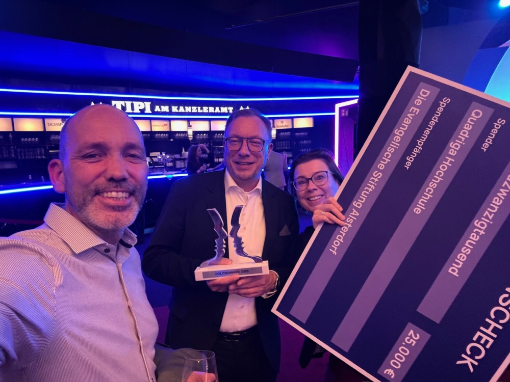Zwei Männer und eine Frau freuen sich über den gewonnen Award und halten einen Check nach oben.
